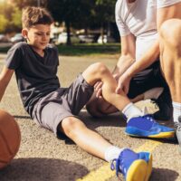 Father helping boy with knee trauma after playing basketball.